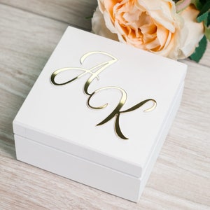 Può includere: Scatola di legno bianca con un'iscrizione in oro corsivo delle lettere "A & K" sul coperchio.