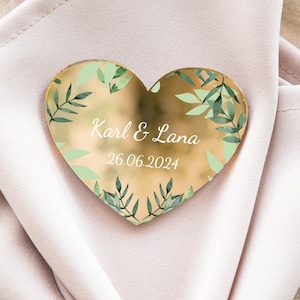 Könnte beinhalten: Goldener herzförmiger Spiegel mit grünem Blattdesign und dem Text "Karl & Lana 26.06.2024".