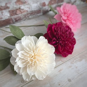 May include: Three paper flowers in different colors: white, pink, and burgundy. The flowers are made of crepe paper and have a realistic appearance.