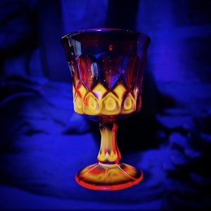 Puede incluir: Una copa de vidrio transparente con un patrón rojo y amarillo. La copa tiene una base ancha y un tallo alto.