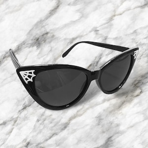 May include: Black cat-eye sunglasses with a spiderweb design on the side of the frames.