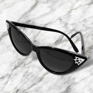 May include: Black cat eye sunglasses with a spider web design on the side of the frames.