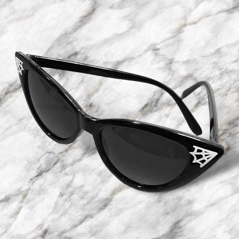 May include: Black cat eye sunglasses with a spider web design on the side of the frames.
