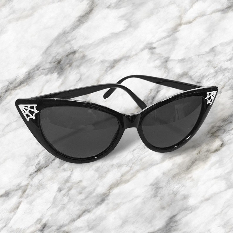 May include: Black cat eye sunglasses with a spiderweb design on the corners of the frames.