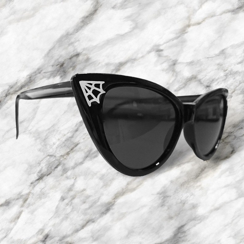 May include: Black cat eye sunglasses with a silver spiderweb design on the frame.