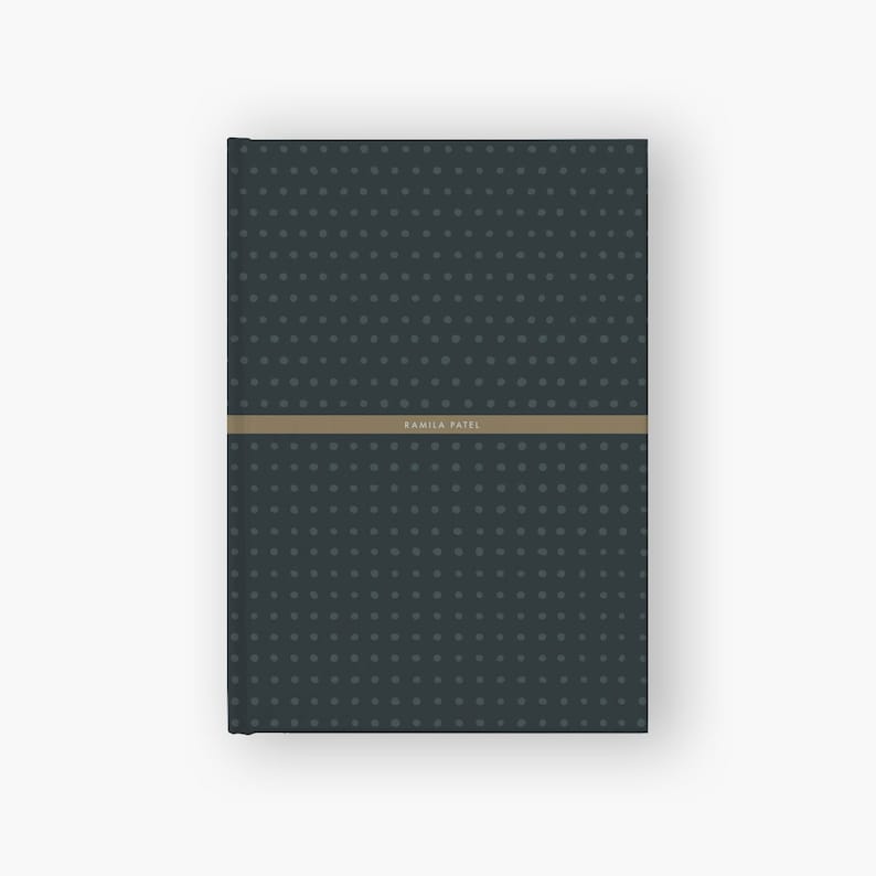 May include: A dark blue notebook with a subtle pattern of small white dots. The notebook has a tan band with the name "Kamila Patel" printed on it.