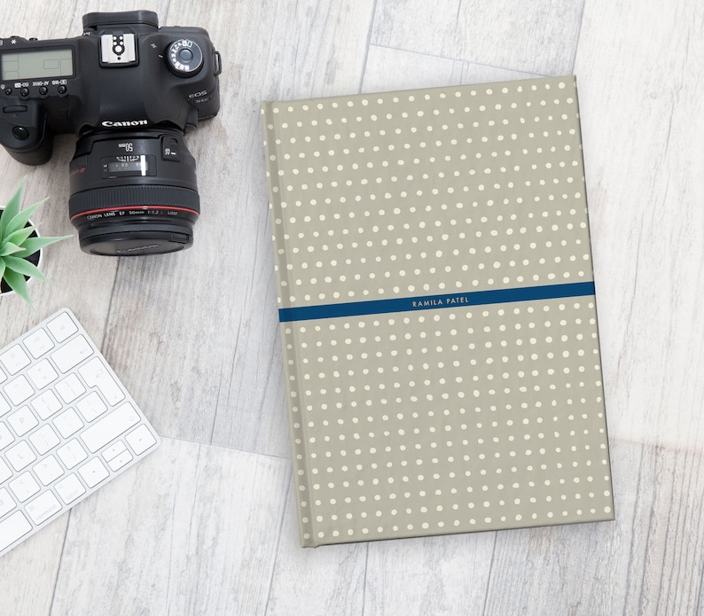 May include: A beige photo album with a white polka dot pattern and a blue ribbon with the name "Ramila Patel" printed on it.