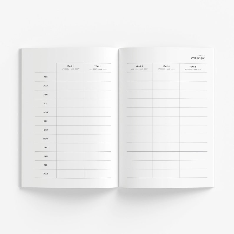 May include: Open white notebook with a minimalist design. The left page lists months from April to March. The right page is labeled "5 Years Overview" and has columns for five years. The notebook is open on a white surface.