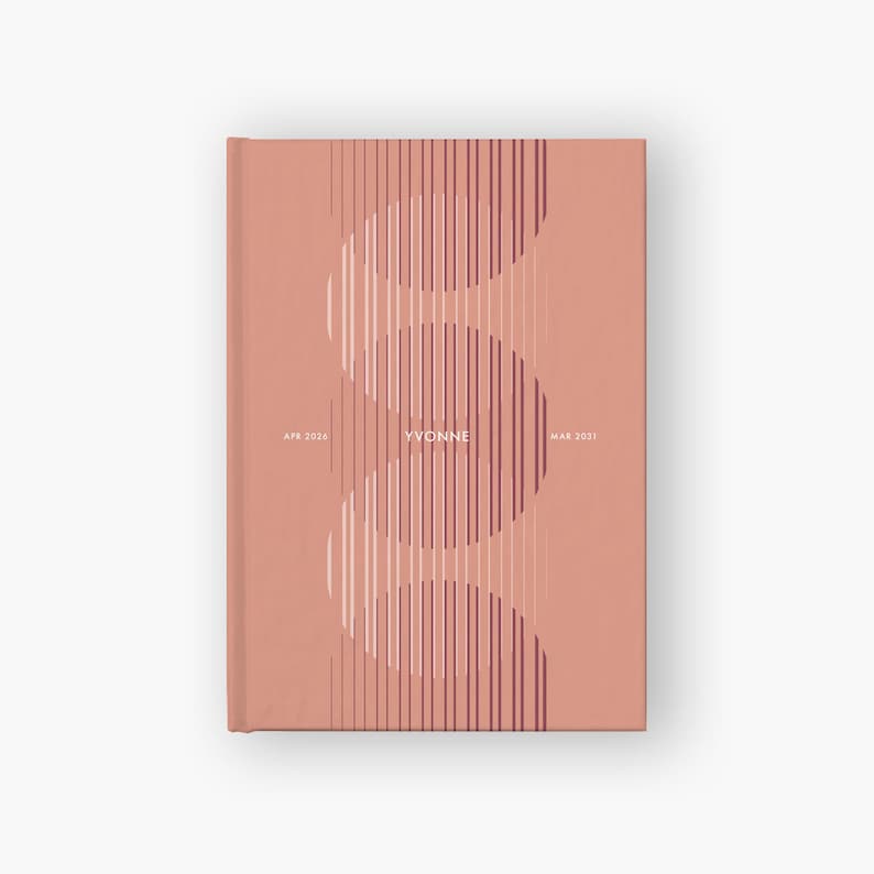 May include: A hardcover journal with a salmon-colored cover. The cover features a vertical design of curved lines in white and burgundy, with the name "YVONNE" in the center. The dates "APR 2026" and "MAR 2031" are also printed on the cover.