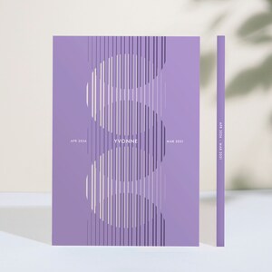 May include: A lavender-colored notebook with a vertical design of white and dark purple lines. The name "YVONNE" is centered, with "APR 2026" and "MAR 2031" on either side. The spine shows "APR 2026 - MAR 2031".