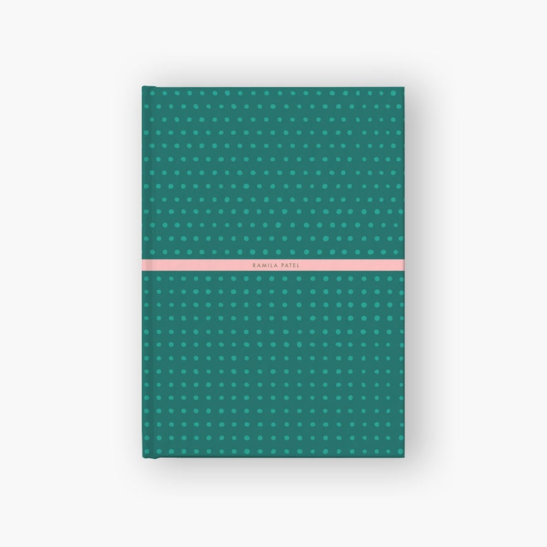 May include: A teal green notebook with a polka dot pattern and a pink stripe with the name "Kamila Patel" printed on it.
