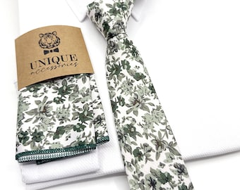 Könnte beinhalten: Ein weißes Hemd mit einem passenden floralen Krawatten- und Einstecktuch-Set. Die Krawatte und das Einstecktuch haben einen weißen Hintergrund mit einem grünen Blumenmuster. Das Set ist von "UNIQUE accessories".