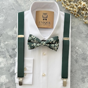 Puede incluir: Una camisa blanca con una pajarita y tirantes verde oscuro. La pajarita presenta un estampado floral. Los tirantes tienen cierres metálicos plateados. Una etiqueta en la camisa dice "UNIQUE accessories".