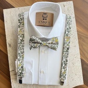 Pode incluir: Uma camisa branca com gravata borboleta e suspensórios a condizer. A gravata borboleta e os suspensórios apresentam um padrão floral com detalhes em verde e amarelo. A camisa tem uma etiqueta que diz "UNIQUE accessories".