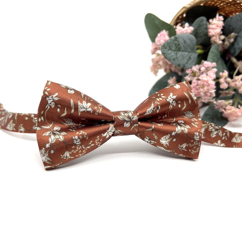 Peut inclure: Un n&oelig;ud papillon marron avec un motif floral blanc. Le n&oelig;ud papillon est en satin et a une forme classique.