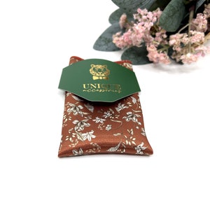 Peut inclure: Un mouchoir de poche marron avec un motif floral blanc. Le mouchoir de poche est pli&eacute; et emball&eacute; dans une bo&icirc;te verte avec un logo de tigre dor&eacute; et le texte "UNIQUE accessories".