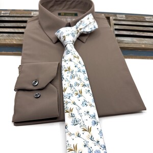 May include: A brown dress shirt with a white and blue floral patterned tie. The tie has a white background with blue and brown floral accents.