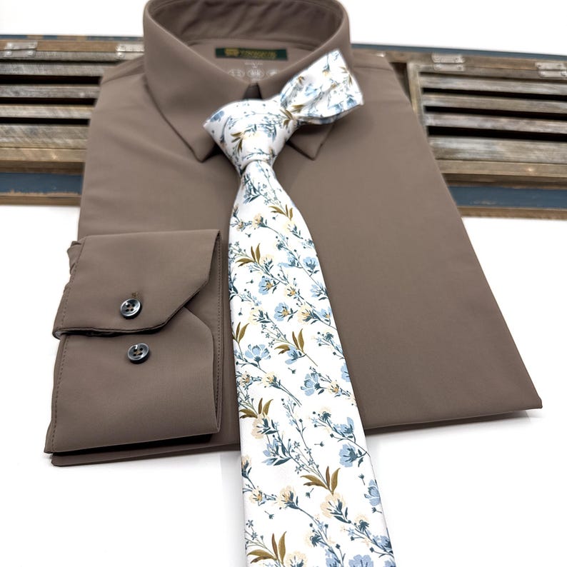 May include: A brown dress shirt with a white and blue floral patterned tie. The tie has a white background with blue and brown floral accents.
