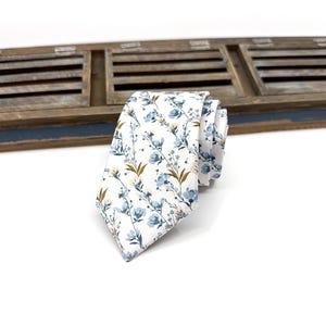 May include: A white necktie with a blue and yellow floral pattern.