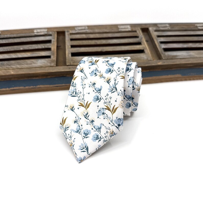 May include: A white necktie with a blue and yellow floral pattern.