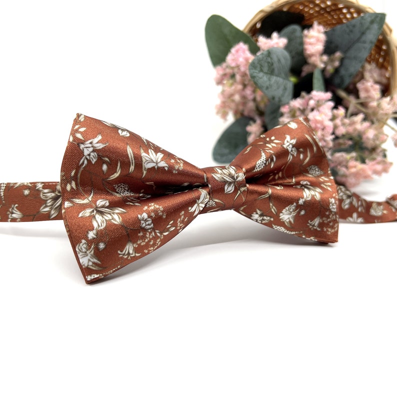 Peut inclure: Un n&oelig;ud papillon marron avec un motif floral blanc. Le n&oelig;ud papillon est en satin et a une forme classique.