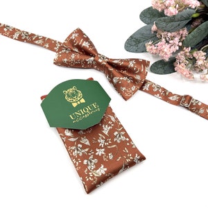 Peut inclure: Un n&oelig;ud papillon marron &agrave; motif floral et un mouchoir de poche assorti. Le mouchoir de poche est pli&eacute; et porte une &eacute;tiquette verte avec le texte "UNIQUE accessories" et un logo de t&ecirc;te de tigre dor&eacute;.