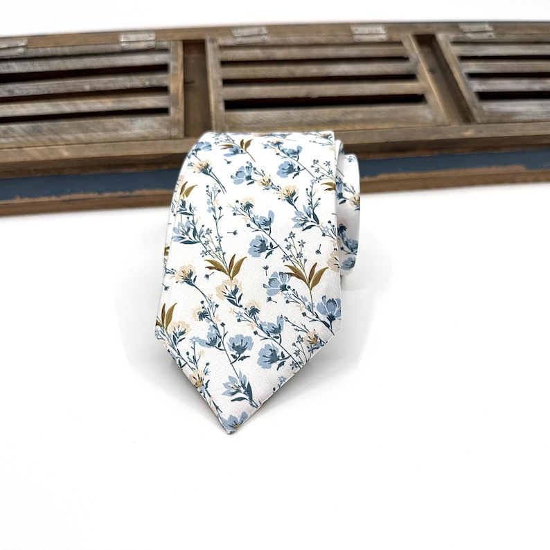 May include: A white necktie with a blue and gold floral pattern.