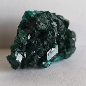 May include: A close-up of a dark teal mineral specimen. The crystalline structure has sharp edges and facets, reflecting light. The mineral's surface has a slightly rough texture, with variations in color and tone. The overall shape is irregular and organic.