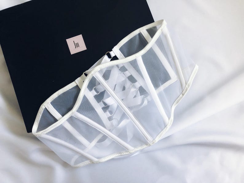 May include: White mesh corset with a lace-up front and a satin trim. The corset is on a white fabric background.
