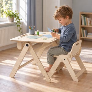 May include: A light-colored wooden activity table and matching chair set with an adjustable frame design. The table surface features a cutout handle and holds a gray pencil cup with colored pencils, a glue stick, and pieces of blue paper.