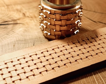 May include: A close-up of a brass leather stamping tool with a woven pattern. The tool is sitting on a piece of leather that has been stamped with the same pattern.