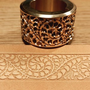 May include: A brass leather stamping tool with a floral design. The tool is used to create a decorative border on leather.