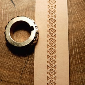 Op de afbeelding: Een messing leder stempelgereedschap met een geometrisch patroon. Het gereedschap wordt gebruikt om een ​​herhalend ontwerp op leer te maken.
