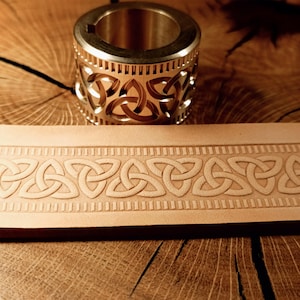 May include: A close-up of a leather strip with a Celtic knot design embossed into the surface. A brass stamp with a similar design is shown above the leather strip.