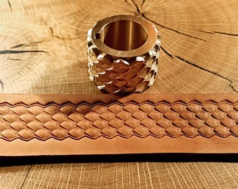 May include: A brass ring with a scale pattern and a brown leather belt with a matching scale design are displayed on a wooden surface. The ring has a cylindrical shape with a hollow center.