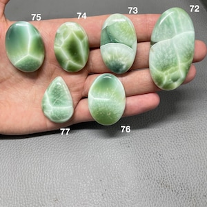 May include: A collection of six polished gemstones in shades of green and white. The stones vary in shape, including oval and teardrop, and feature unique veining patterns. The gemstones are displayed against a neutral background.