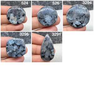 Op de afbeelding: Een collectie van vijf gepolijste labradoriet edelstenen met blauwe iriserende flitsen, donkergrijze en zwarte insluitingen en kristallijne texturen. De stenen zijn gelabeld met de nummers 524, 526, 3294, 3296 en 3291, in ronde, vierkante en druppelvormen.