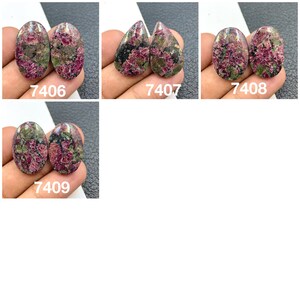 Może przedstawiać: Cztery pary owalnych i kroplowatych kamieni szlachetnych w szlifie kaboszonowym. Kamienie są połączeniem różowego, zielonego i czarnego z marmurowym wzorem. Kamienie są oznaczone numerami 7406, 7407, 7408 i 7409.