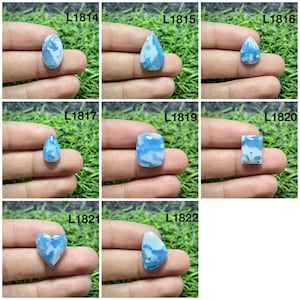 May include: A collection of eight polished blue and white gemstones labeled L1814 through L1822. Each stone features a unique cloud-like pattern in shades of sky blue and opaque white, presented in various shapes including oval, pear, heart, and rectangular.