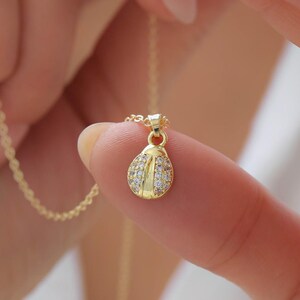 Puede incluir: Un colgante dorado con forma de mariquita, que presenta una cabeza de oro pulido y alas incrustadas con pequeñas piedras transparentes y brillantes. El colgante está unido a una cadena dorada fina y delicada, creando un collar refinado.