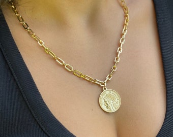 Puede incluir: Un collar de cadena de oro con un gran colgante de moneda de oro que presenta el perfil de la cara de una mujer. El collar lo lleva una persona con una camisa negra.