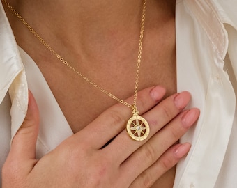 May include: A gold chain necklace with a compass pendant featuring a small clear stone in the centre. The compass is surrounded by small stones.