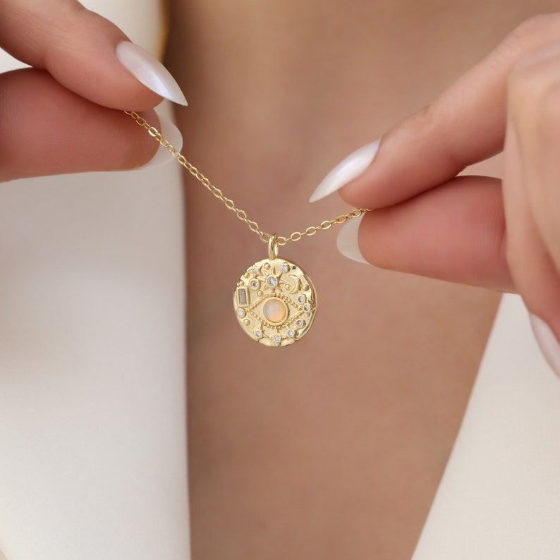 May include: Gold necklace with a round pendant featuring an opal eye surrounded by small clear stones and a textured design.