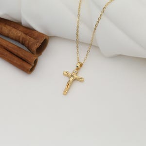 May include: A gold chain necklace with a small gold cross pendant featuring a detailed figure of Jesus Christ.