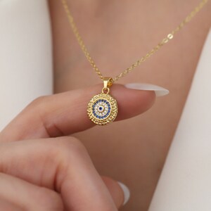 May include: Gold necklace with a blue and white evil eye pendant. The pendant is surrounded by small clear stones.