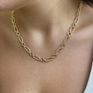 May include: A gold chain necklace with a delicate, textured design. The chain is made of oval links and is worn around the neck.