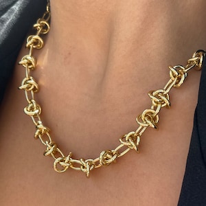 Peut inclure: Un collier en cha&icirc;ne dor&eacute;e avec un design nou&eacute;. La cha&icirc;ne est &eacute;paisse et a un aspect &eacute;pais.
