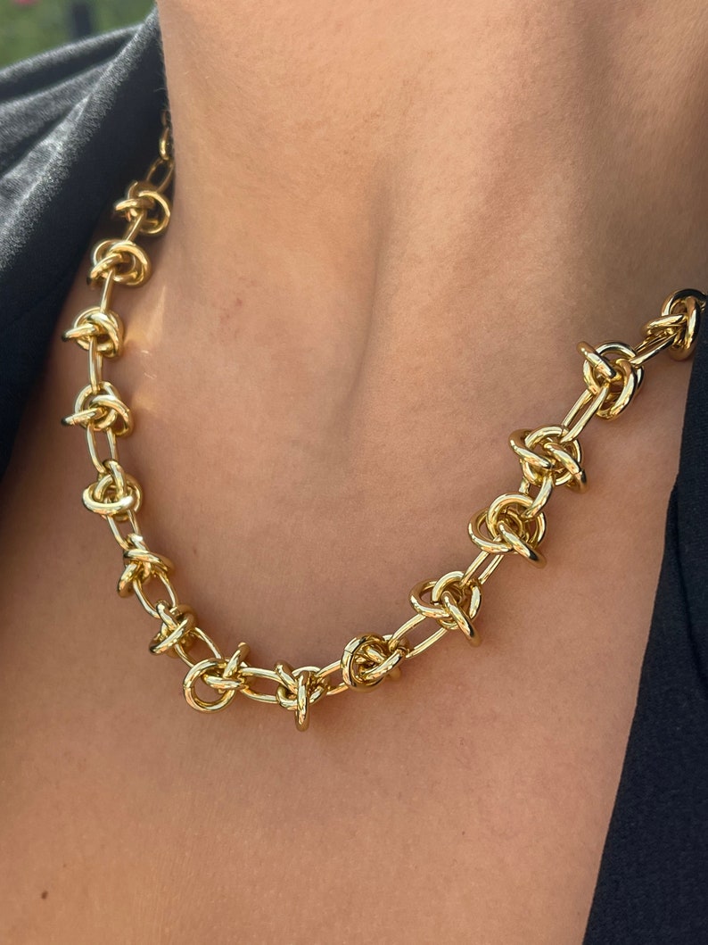 Peut inclure: Un collier en cha&icirc;ne dor&eacute;e avec un design nou&eacute;. La cha&icirc;ne est &eacute;paisse et a un aspect &eacute;pais.