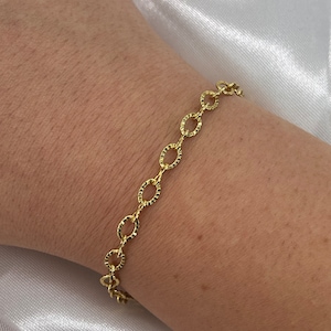 May include: A gold chain bracelet with a textured, oval-shaped link design.