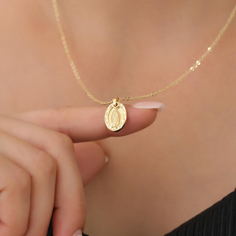 Pode incluir: Um colar de corrente de ouro com um pequeno pingente oval com uma imagem da Virgem Maria.